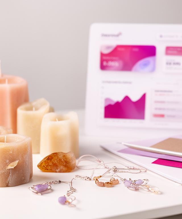 Handmade candles and jewellery arranged beside a profit dashboard on a studio desk