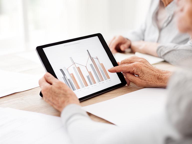 Older adult using a tablet while reviewing retirement income charts at a bright table